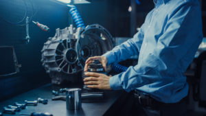 Closeup of a torso of an automotive engineer in a blue dress shirt. He is putting together a transmission gear for a vehicle.